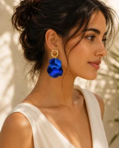 Woman styling blue statement earrings with a simple neutral neckline and swept-back hairstyle.
