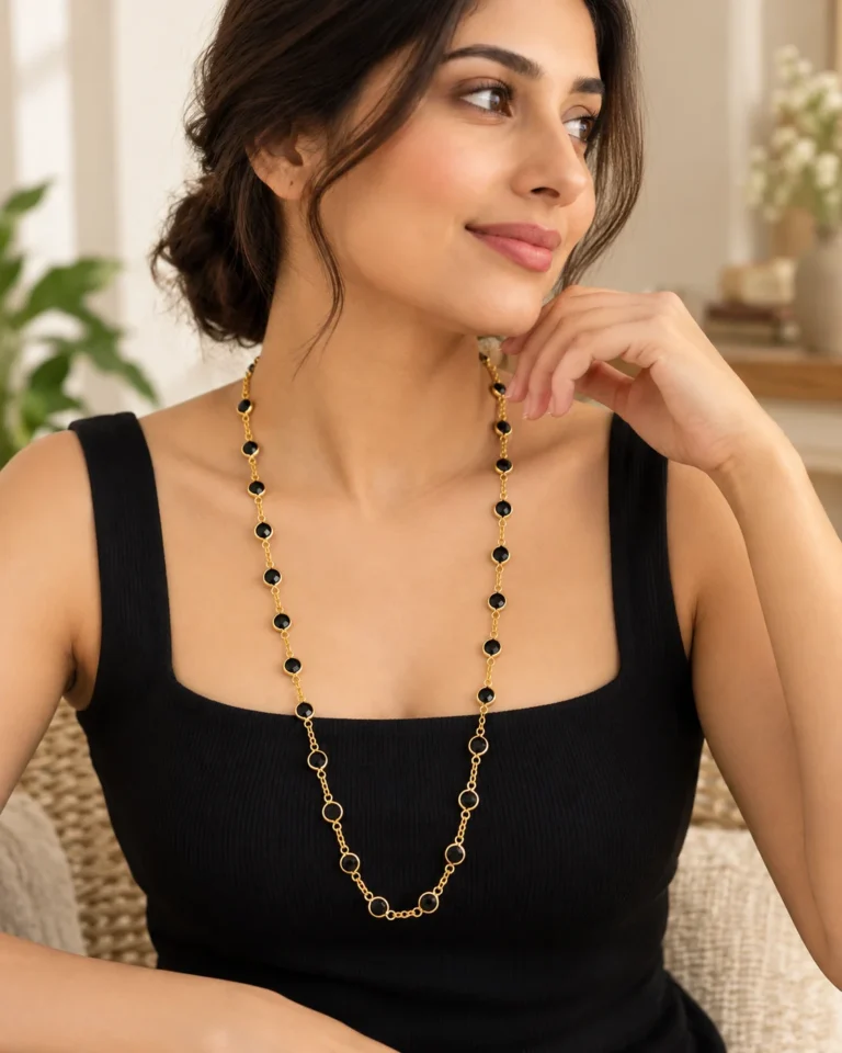 Long gold-tone stone-studded chain styled against a simple black square-neck top.